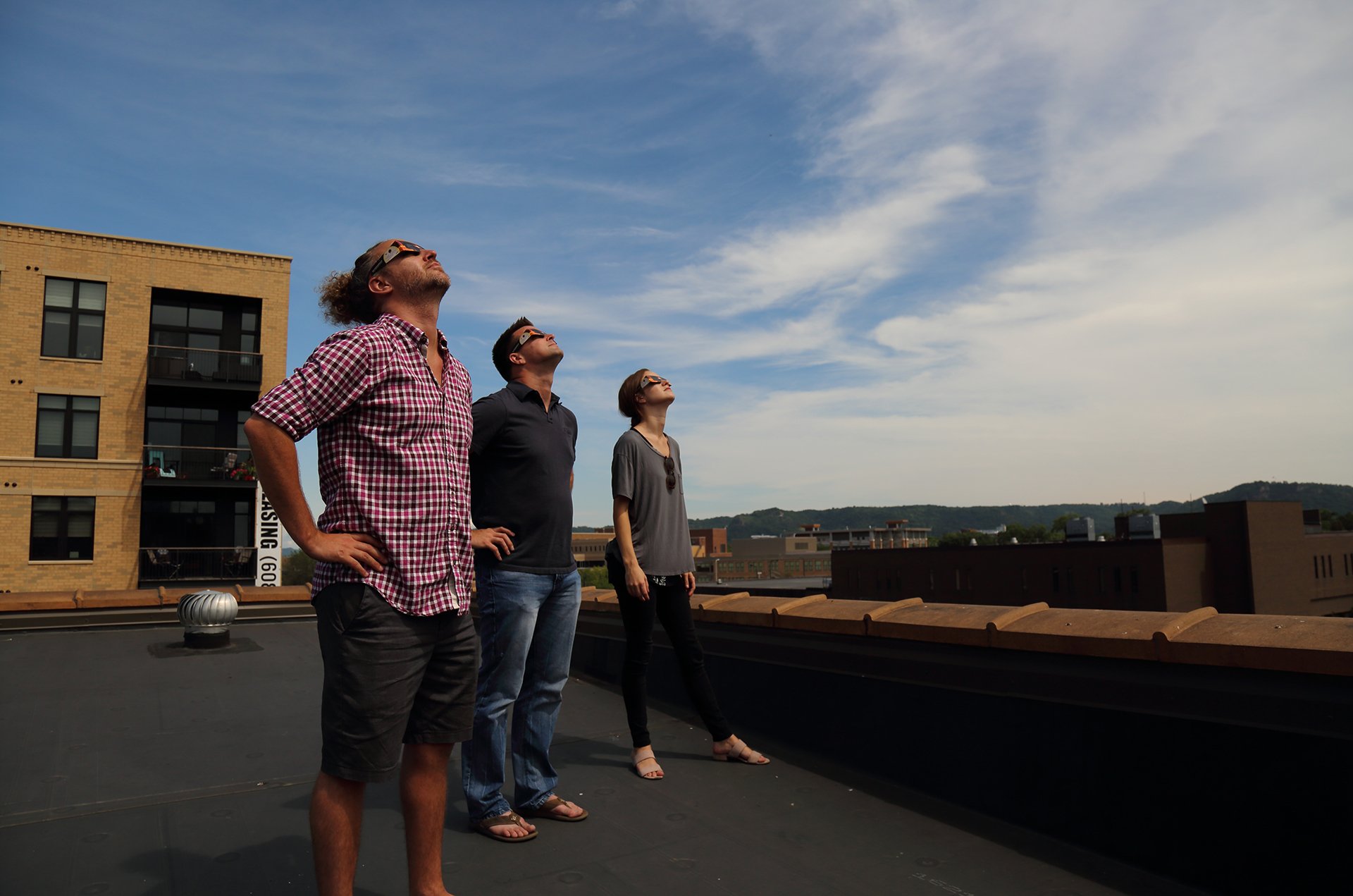 Three Vendi Advertising team members wearing eclipse glasses and viewing a solar eclipse from Vendi’s roof in 2017