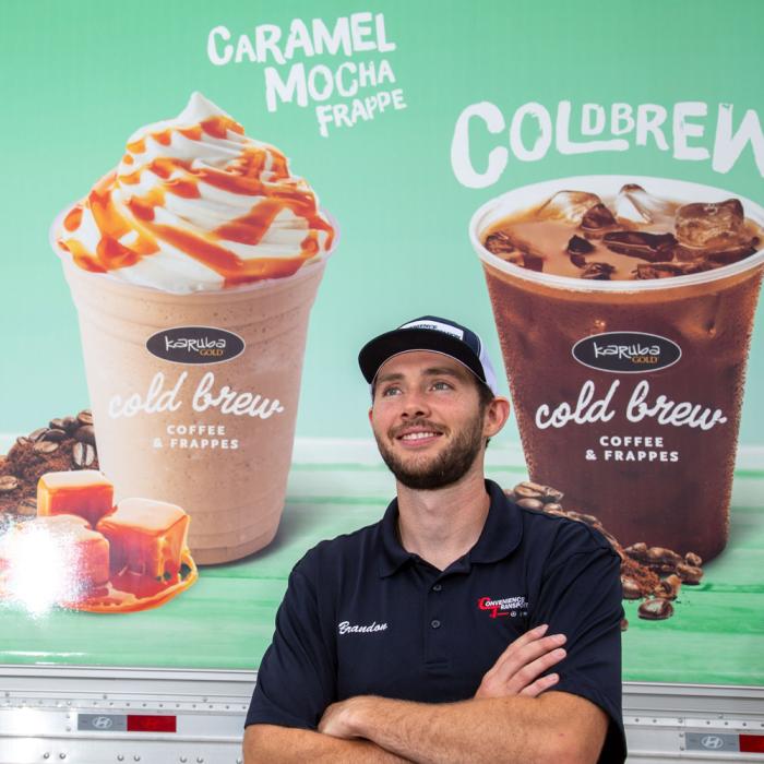 Kwik Trip driver with arms crossed, smiling and standing next to a KT semi advertising KT’s cold and frozen drinks