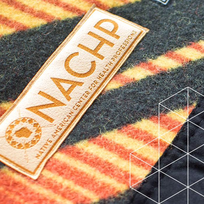 In the background, and orange, yellow and black striped cloth. Resting on top is  a leather strip saying "NACHP" and under it says "Native American Center for Health Professions"