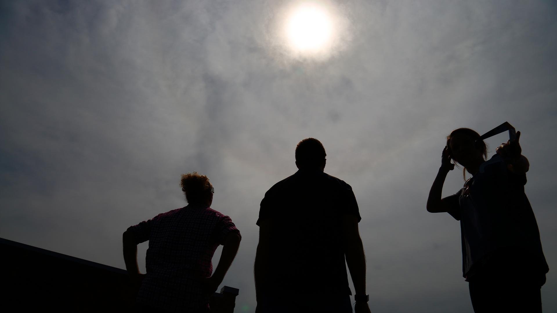 Silhouettes of three Vendi Advertising team members photographed from behind viewing a solar eclipse from the Vendi roof