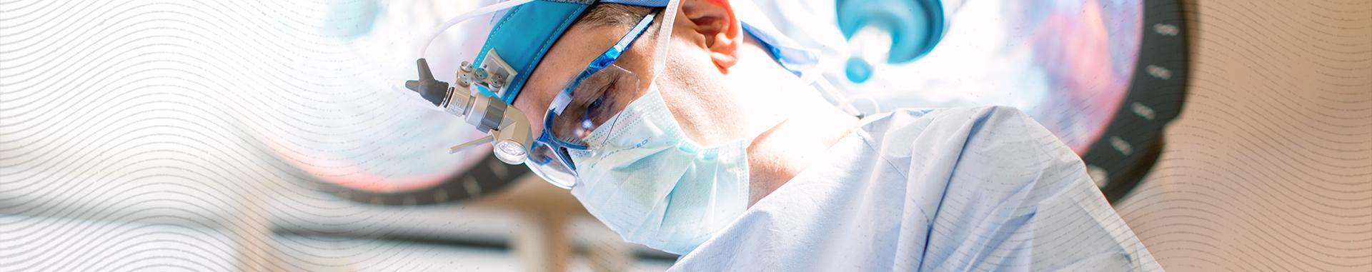 A surgeon looks down with a surgical light behind him. 